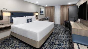 Une chambre d’hôtel avec un grand lit, un bureau avec une chaise, un téléviseur à écran plat et un téléviseur fixé au mur.