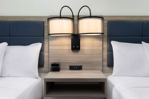 Una habitación de hotel con dos camas, una mesita de noche, una lámpara y un enchufe.