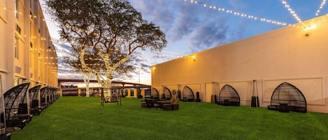 A courtyard with a green lawn, seating areas, and string lights.