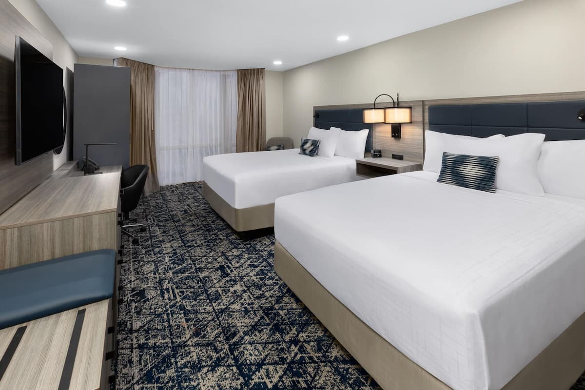 A hotel room with two beds, a TV, a desk, and a chair.
