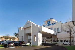 A modern building with a prominent 'WYNDHAM' sign, a parking lot, and a flagpole. - Wyndham DFW Airport (Irving)