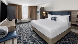A hotel room with a large bed, a desk with a chair, a television, and a window with curtains. - Wyndham DFW Airport (Irving)