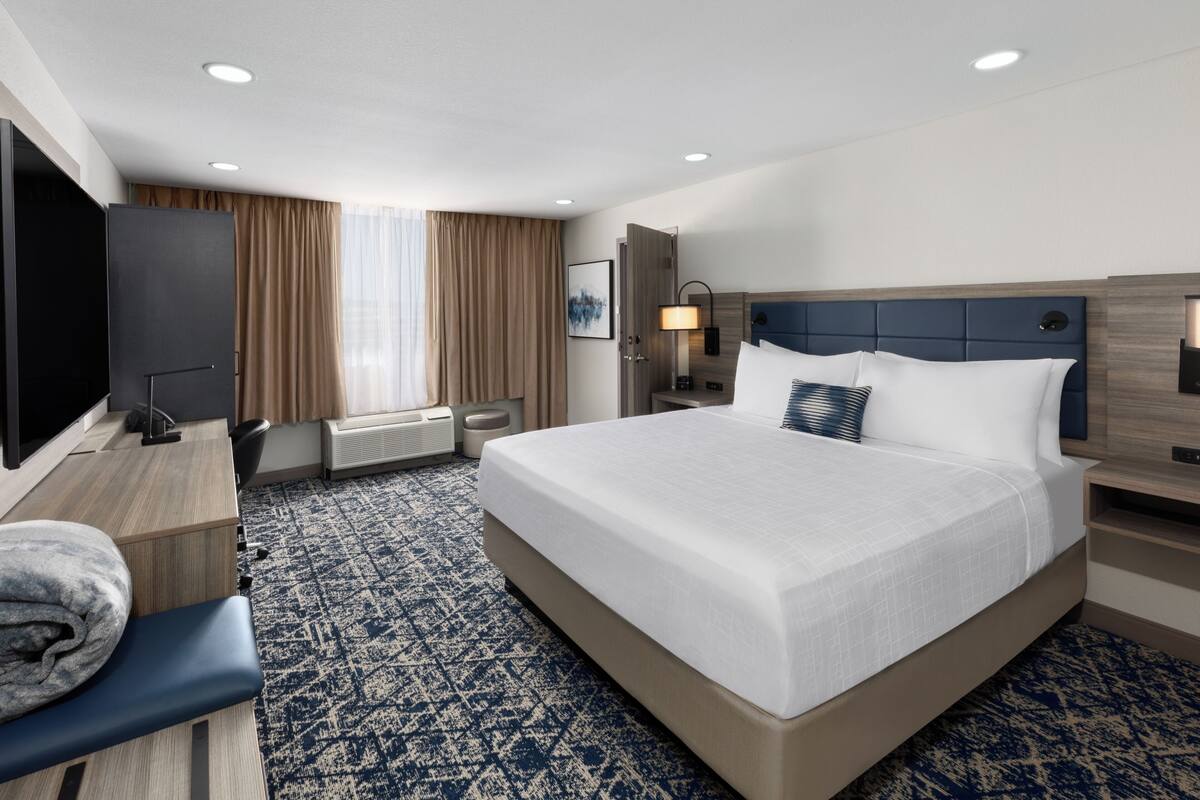 A hotel room with a large bed, a desk with a chair, a television, and a window with curtains.