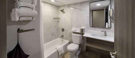 A modern bathroom with a bathtub, toilet, and sink. There are towels hanging on a rack and a hair dryer on the wall.