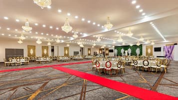 A banquet hall with round tables, gold chairs, and chandeliers.