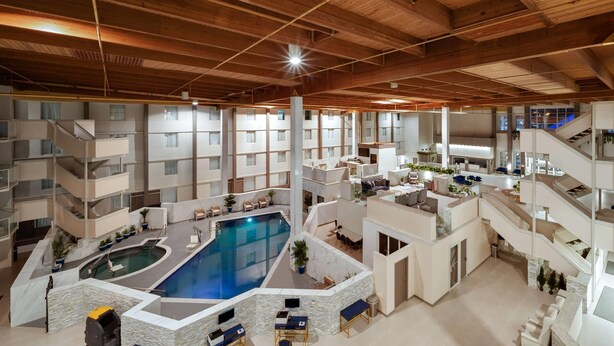 A multi-level indoor complex with a central swimming pool, multiple balconies, and various seating areas. - Wyndham DFW Airport (Irving)