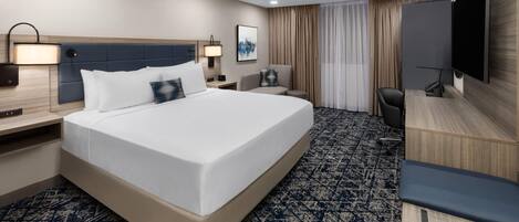 A hotel room with a large bed, a desk, a chair, a TV, and a window with curtains.