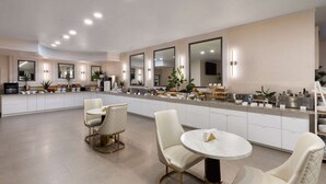 A modern kitchen with white cabinetry, a central island, and two round tables with chairs. - Wyndham DFW Airport (Irving)