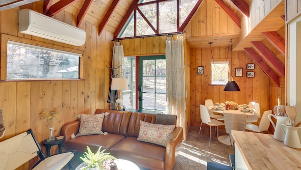 L’intérieur chaleureux d’un chalet, avec un revêtement mural en bois, un coin repas et un canapé agrémenté de coussins.