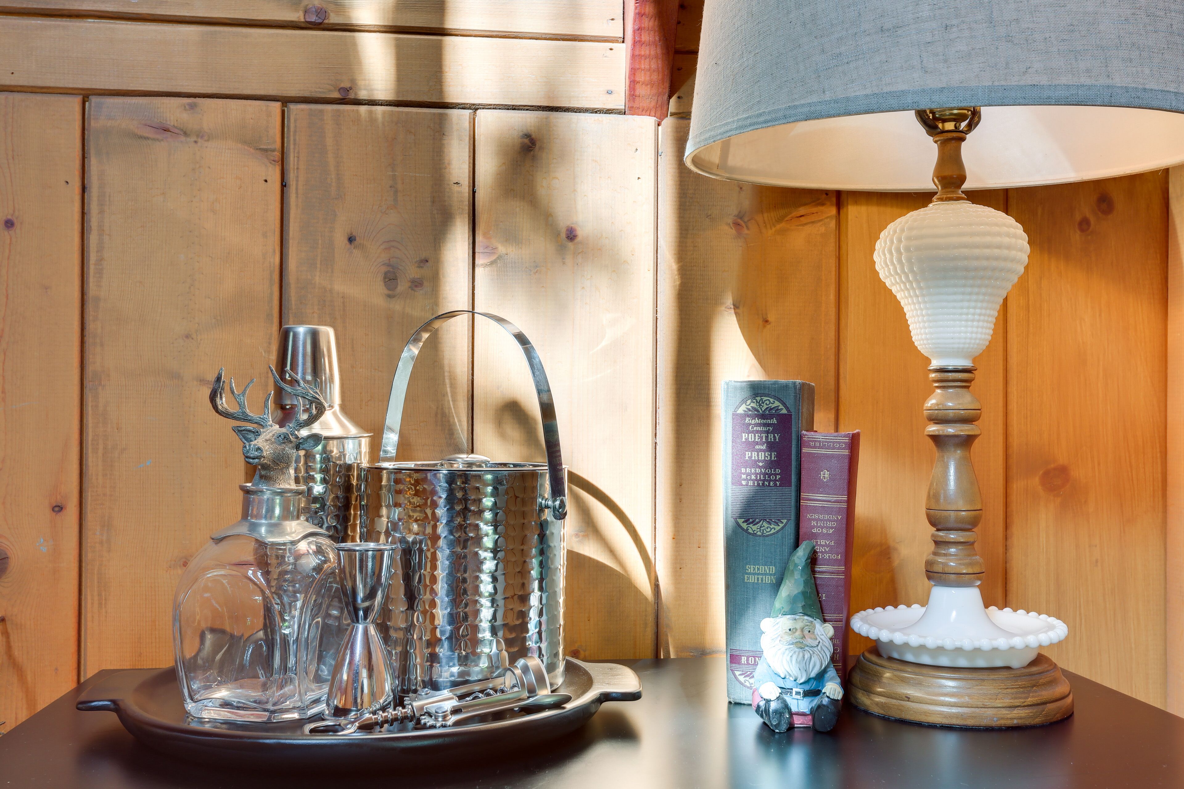 A table with a glass decanter set, a lamp, and books.
