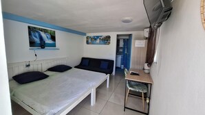 Ein Schlafzimmer mit Bett, Schlafsofa, Schreibtisch und Stuhl. An der Wand hängt ein Gemälde, ein Fenster und eine Klimaanlage sind vorhanden.