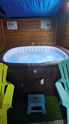 Un bain Ă remous avec un mur en bois en arriĂšre-plan, un petit marchepied et deux chaises.