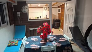 Ein Essbereich mit einem Tisch für zwei Personen, einem blauen Sofa, einem kleinen Tisch mit einer Vase roter Blumen und einer Küche im Hintergrund.