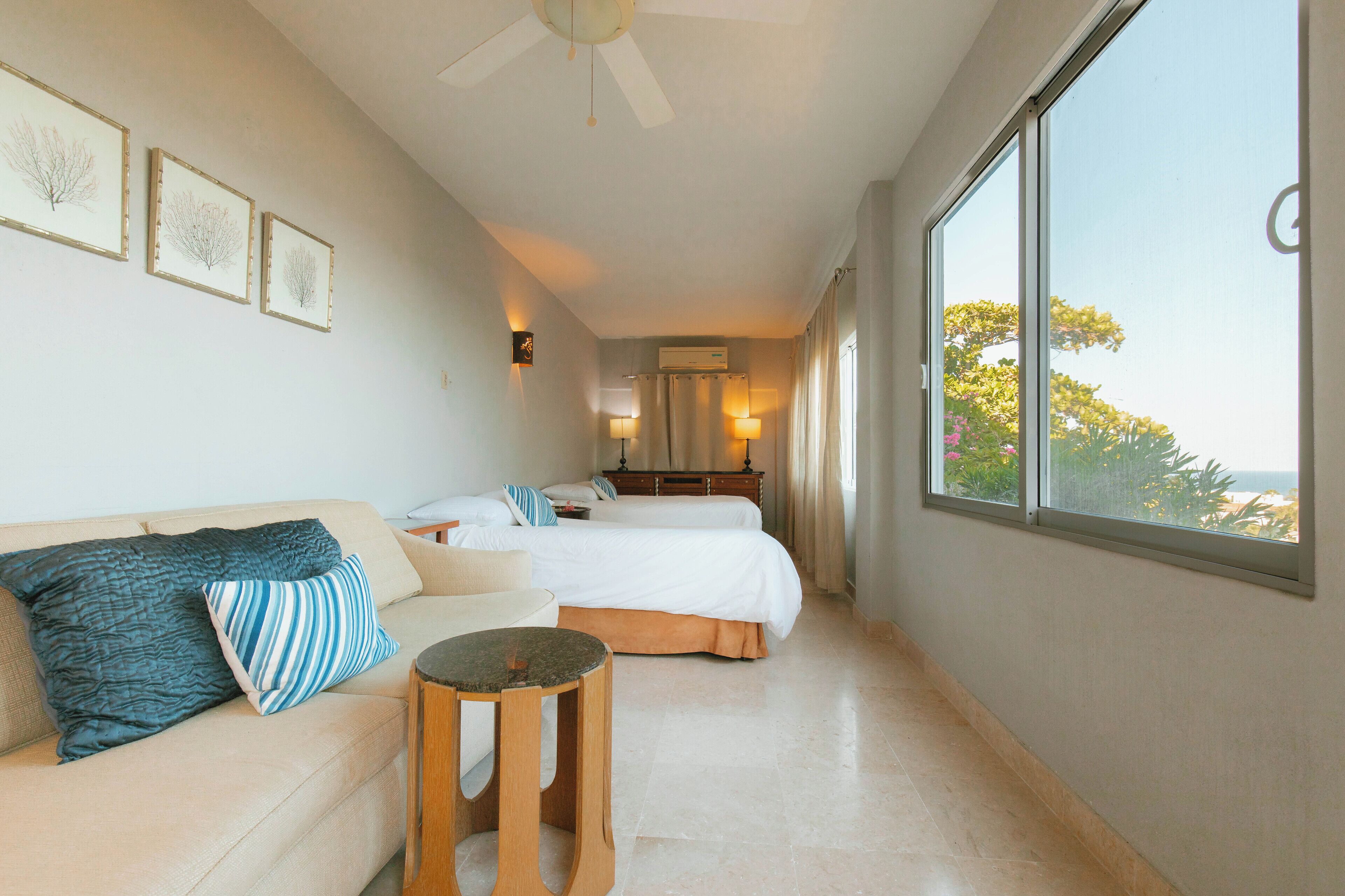 A hotel room with a bed, a sofa, a small table, and a large window offering a view of the outdoors.
