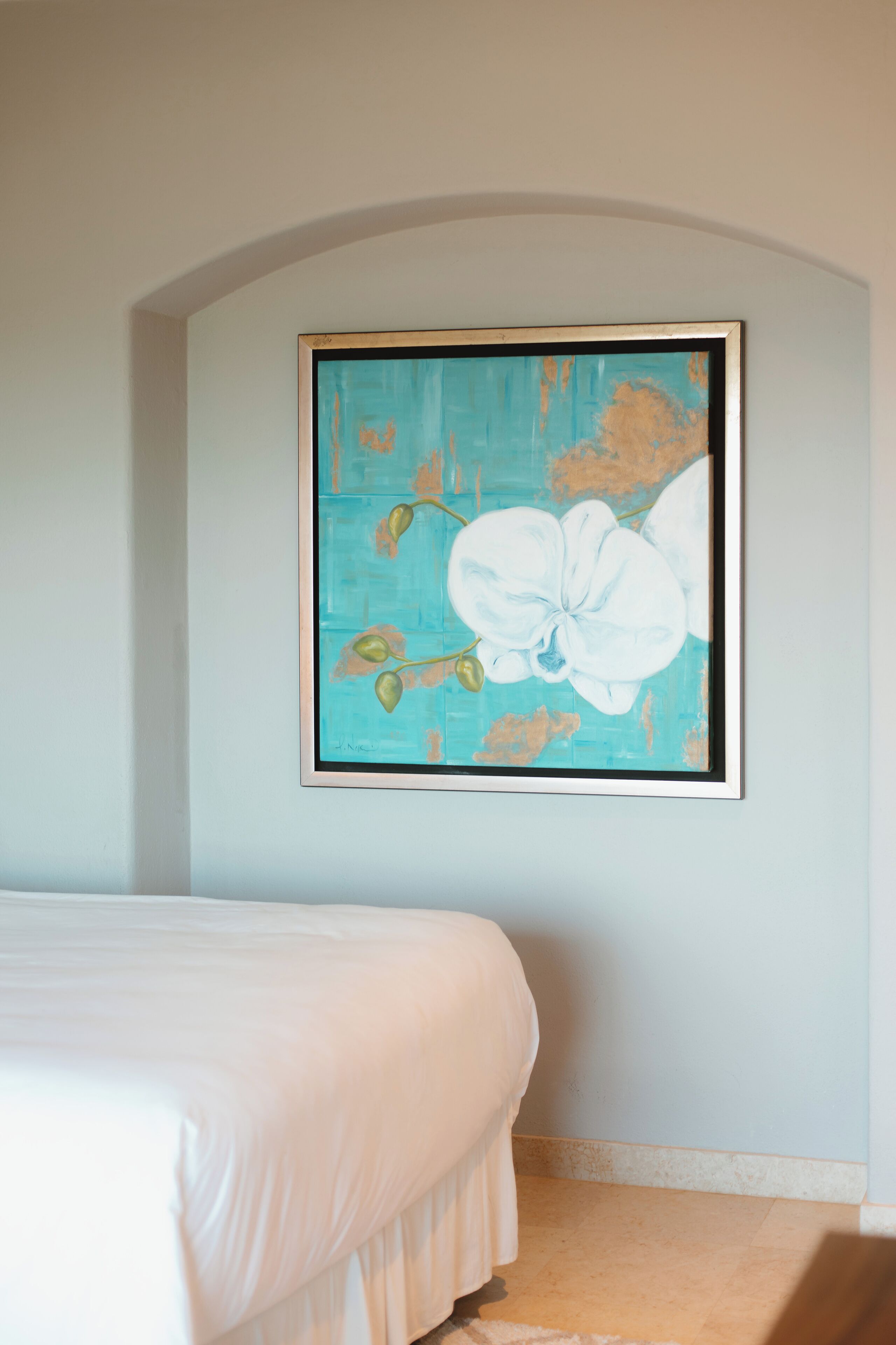 A bedroom with a bed, a wall-mounted painting of a flower, and a light blue wall.