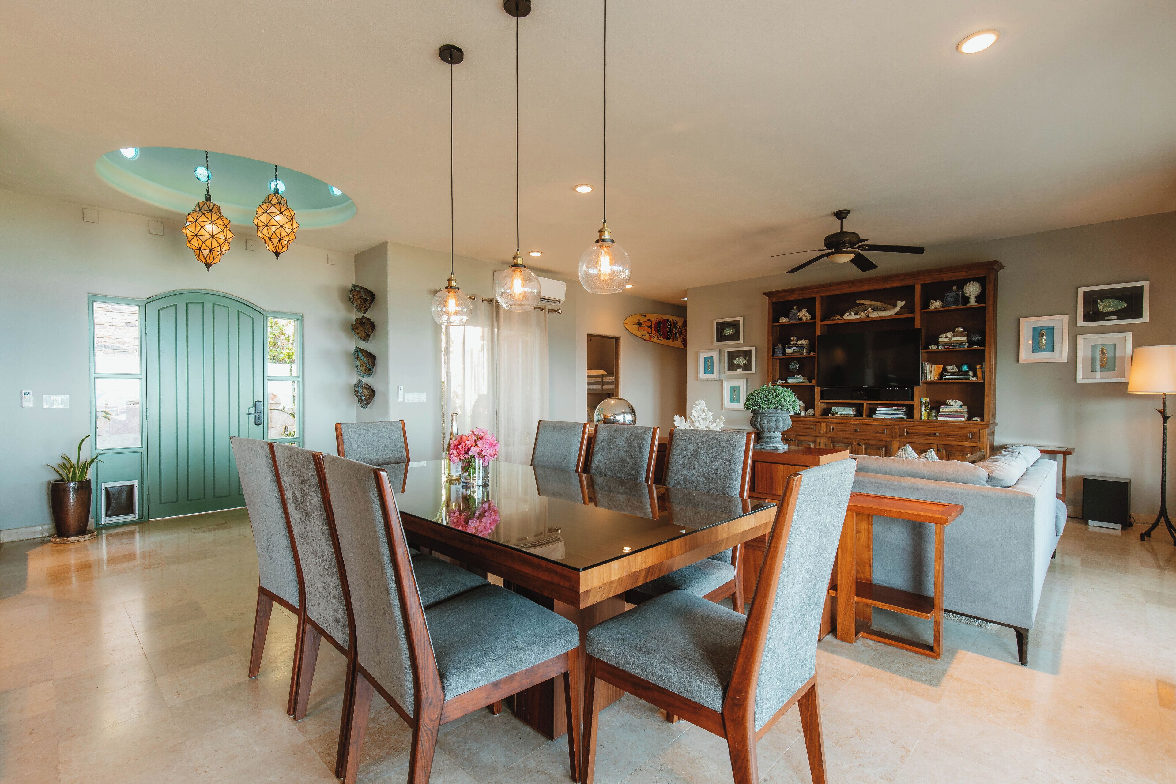 A spacious dining area with a wooden table and chairs, a ceiling fan, and a living area with a sofa and TV.