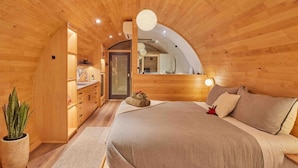 Une chambre confortable avec un plafond en bois, un grand lit, une table de chevet et une plante en pot.