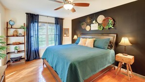 A bedroom with a bed, a ceiling fan, a nightstand with a lamp, a window with curtains, and a shelf with decorative items. - Virginia Escape w/ Patio & Fire Pit, Near Hiking! (Wytheville)