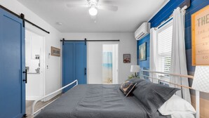 Una camera da letto con un letto, una ventola a soffitto, una finestra con tende e un condizionatore d'aria a parete.