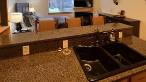 Eine moderne Küche mit Granit-Arbeitsplatten, einem integrierten Herd und einer großen Kochinsel mit Spüle. Es gibt einen Essbereich mit Tisch und Stühlen sowie einen an der Wand montierten Fernseher.