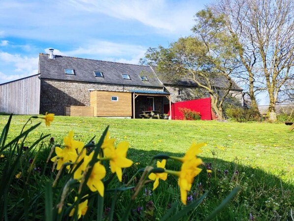 Une ferme rustique avec une façade en pierre, une extension en bois et une clôture rouge.