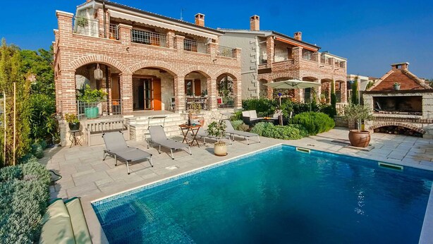 Una casa grande de ladrillo con piscina, mobiliario exterior y zona de barbacoa.