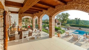 Un patio techado al aire libre con piscina, paredes de piedra y vigas de madera.