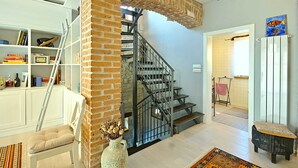 Una escalera con un muro de ladrillo, una estantería blanca, un banco acolchado y un banco de mimbre.