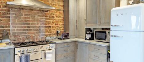 A kitchen with a brick wall, stainless steel appliances, wooden cabinets, and a white refrigerator.