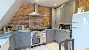 A kitchen with a brick wall, a gas stove, an oven, a microwave, and a refrigerator. - Thomond House, Midhurst -  a flat that sleeps 4 guests  in 2 bedrooms (Midhurst)