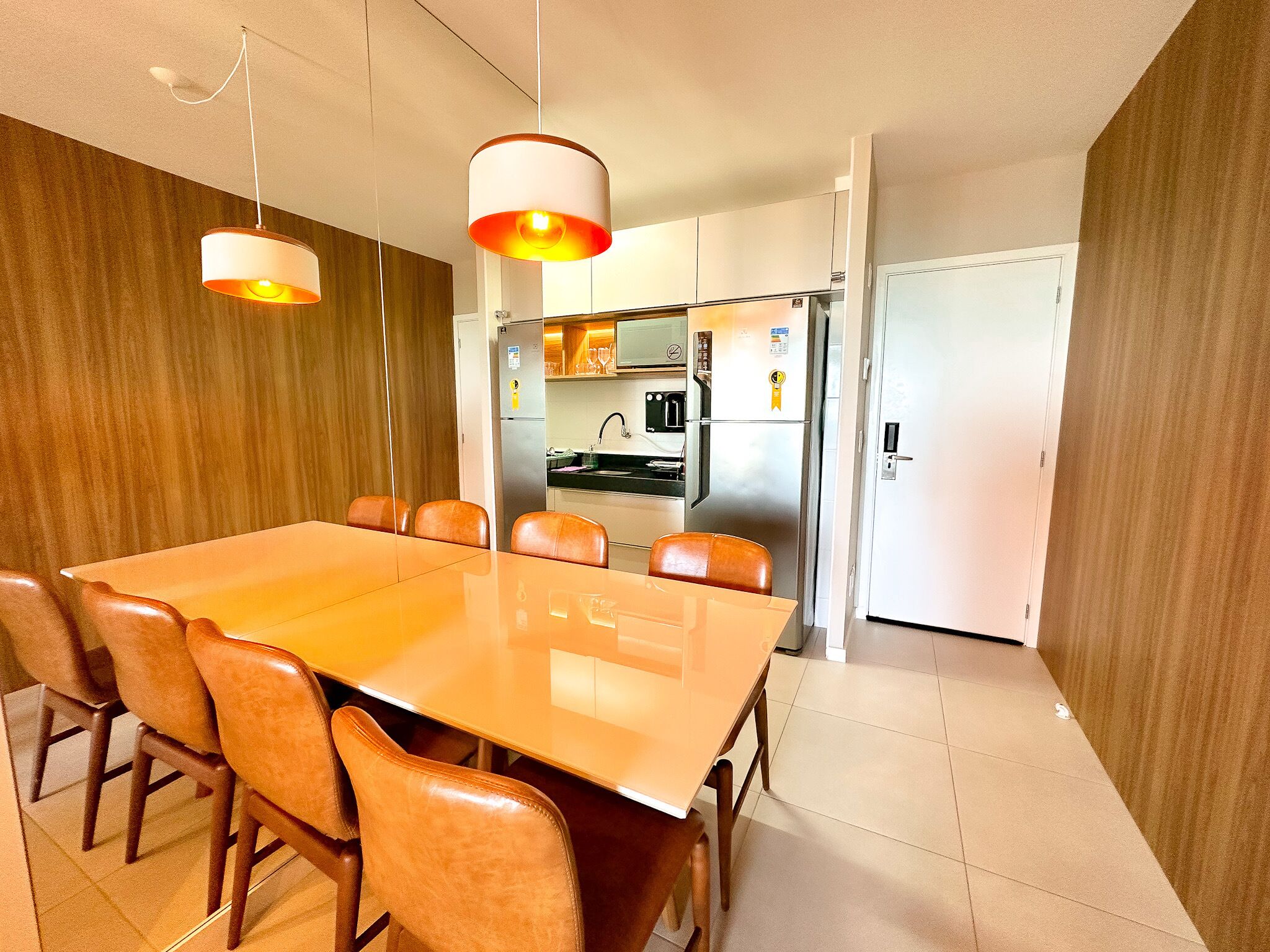Un comedor moderno con una larga mesa y seis sillas, una cocina con electrodomésticos de acero inoxidable y una pared decorativa de madera.