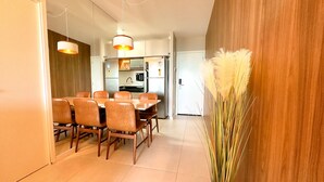 A modern kitchen with stainless steel appliances, a dining area with a wooden table and chairs, and a decorative plant. - Edifício Time (Maceió)
