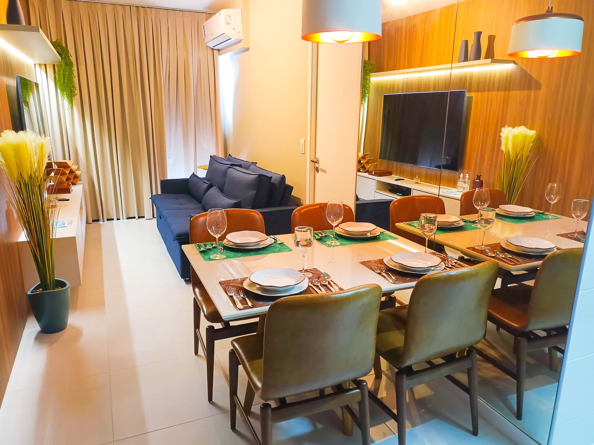 Una sala de estar moderna con un sofá, una mesa de comedor preparada para cuatro comensales y un televisor de pantalla plana montado en la pared.