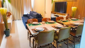 A modern living room with a sofa, dining table set for four, and a flat-screen TV mounted on the wall. - Edifício Time (Maceió)