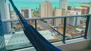 A cityscape with a view of the ocean, buildings, and a hammock on a balcony. - Edifício Time (Maceió)
