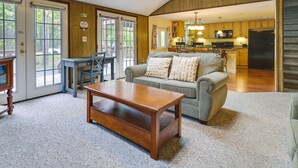 Un salón amplio con una mesa de centro de madera, un sofá con cojines estampados y una zona de comedor con mesa y sillas.