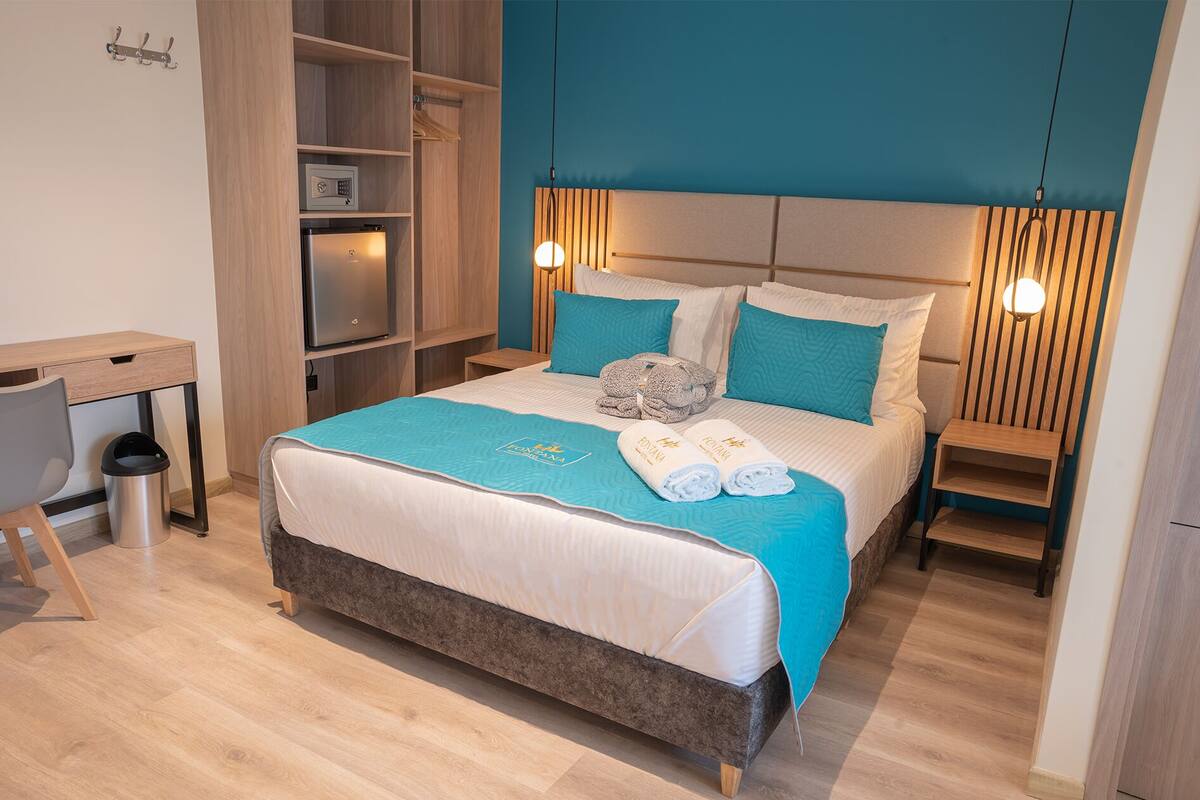 A hotel room with a bed, a desk, a trash bin, and a wardrobe.
