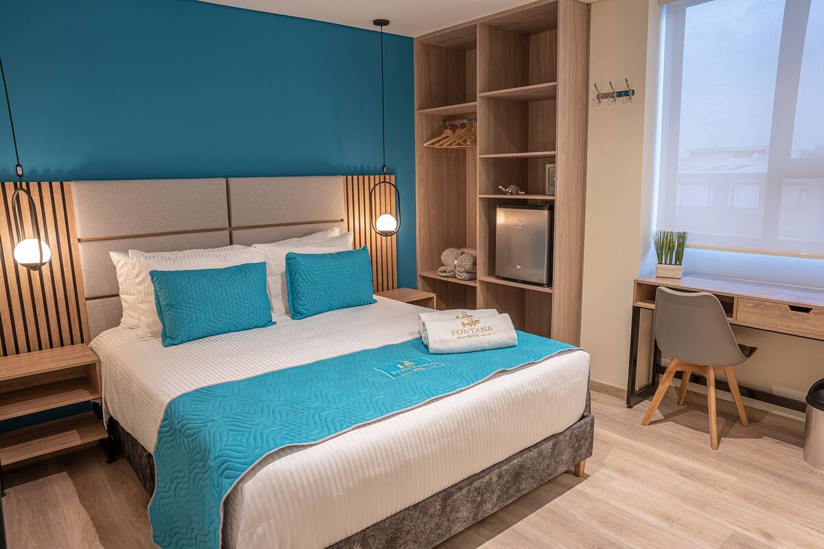 A modern hotel room with a large bed, a desk, and a wardrobe.
