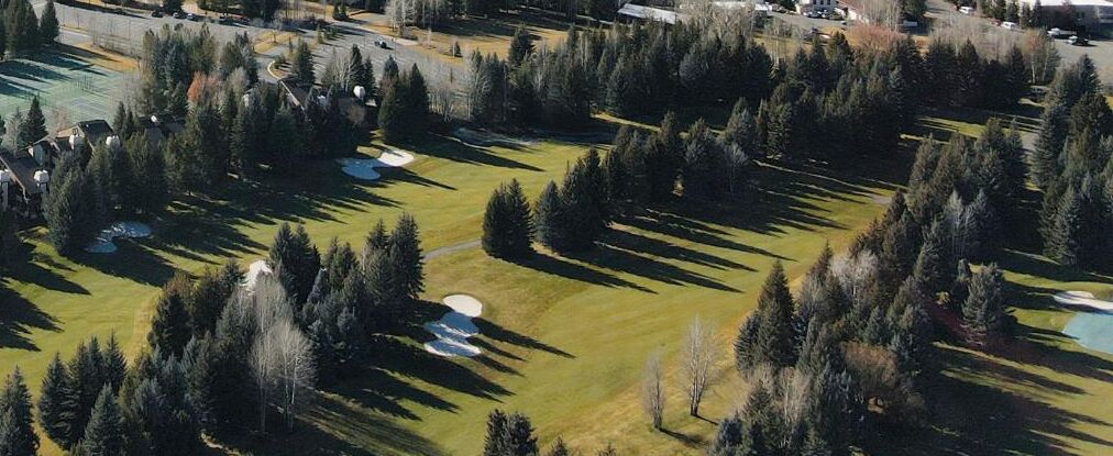 Vue aérienne d’un parcours de golf avec de nombreux bunkers et une forêt dense qui l’entoure.
