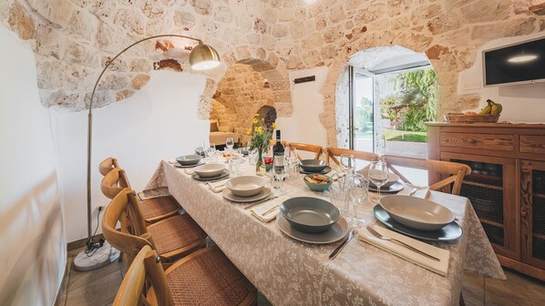 Un comedor con pared de piedra, una mesa larga dispuesta para seis personas y un televisor montado en la pared.