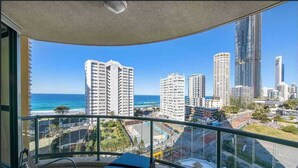 Un balcon offrant une vue sur l’océan et sur le paysage urbain, notamment sur les immeubles de grande hauteur.