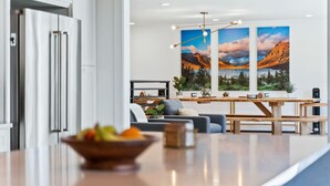 A modern kitchen with a large island, a dining area with a wooden table and benches, and two large landscape paintings on the wall.
