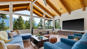 A spacious living room with a large TV, comfortable seating, and a view of mountains.