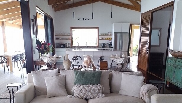 Una sala de estar moderna con un sofá seccional color beige, una mesa de centro y un televisor. La habitación tiene vigas de madera en el techo y un ventanal grande.