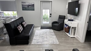 Een moderne woonkamer met een zwarte leren bank, een grijze fauteuil en een televisie op een witte dressoir.