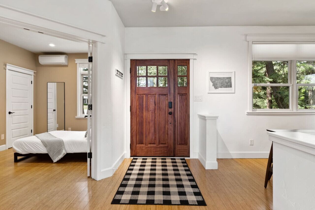 Une chambre à coucher avec un lit, un tapis à carreaux, une porte en bois et une fenêtre donnant sur des arbres.