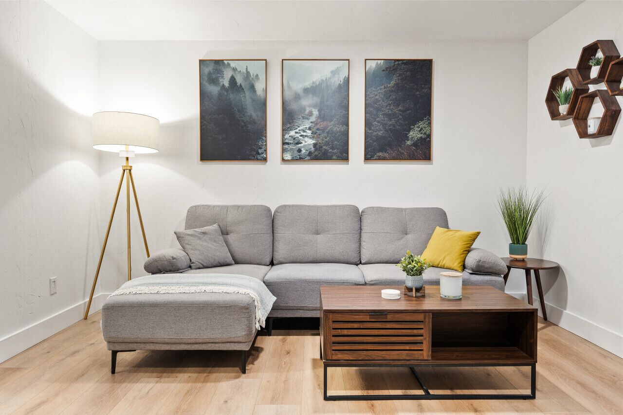 A living room with a grey sofa, a wooden coffee table, a floor lamp, and three framed pictures on the wall.