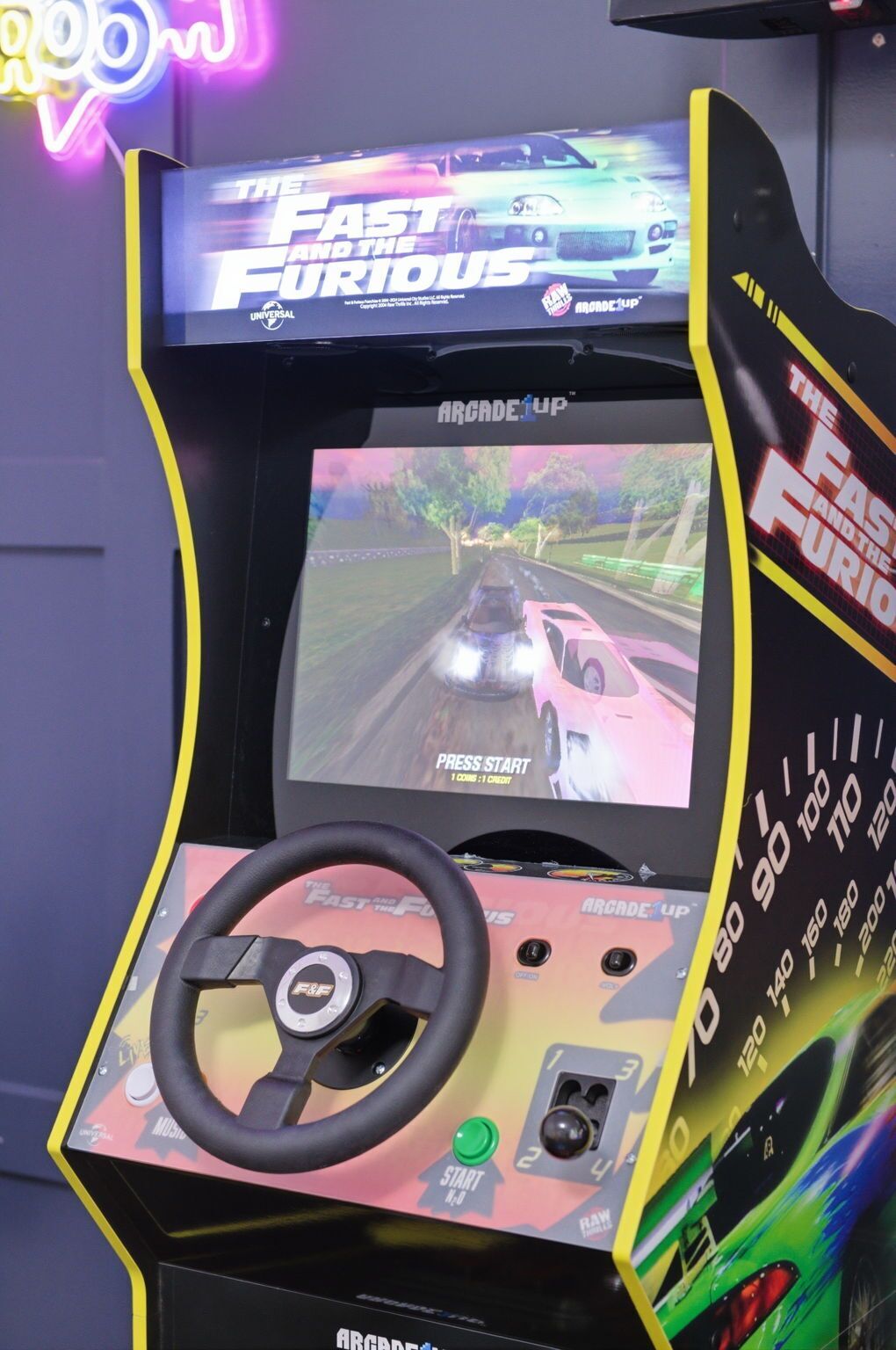 Una macchina arcade per giochi di corse, dotata di volante, schermo che mostra un gioco di guida e insegna luminosa sullo sfondo.