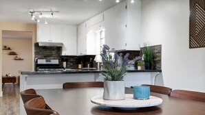 A modern kitchen with white cabinets, a central island, and a dining area with wooden chairs. - Glacier Getaway! Huge Home! Sleeps 14! (Columbia Falls)