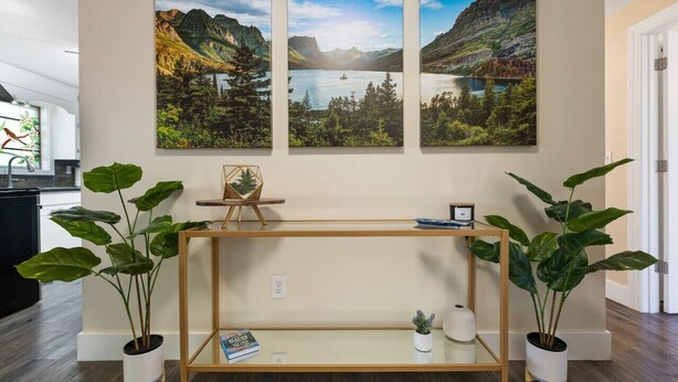 A room with a wooden console table, potted plants, and three landscape paintings on the wall. - Glacier Getaway! Huge Home! Sleeps 14! (Columbia Falls)